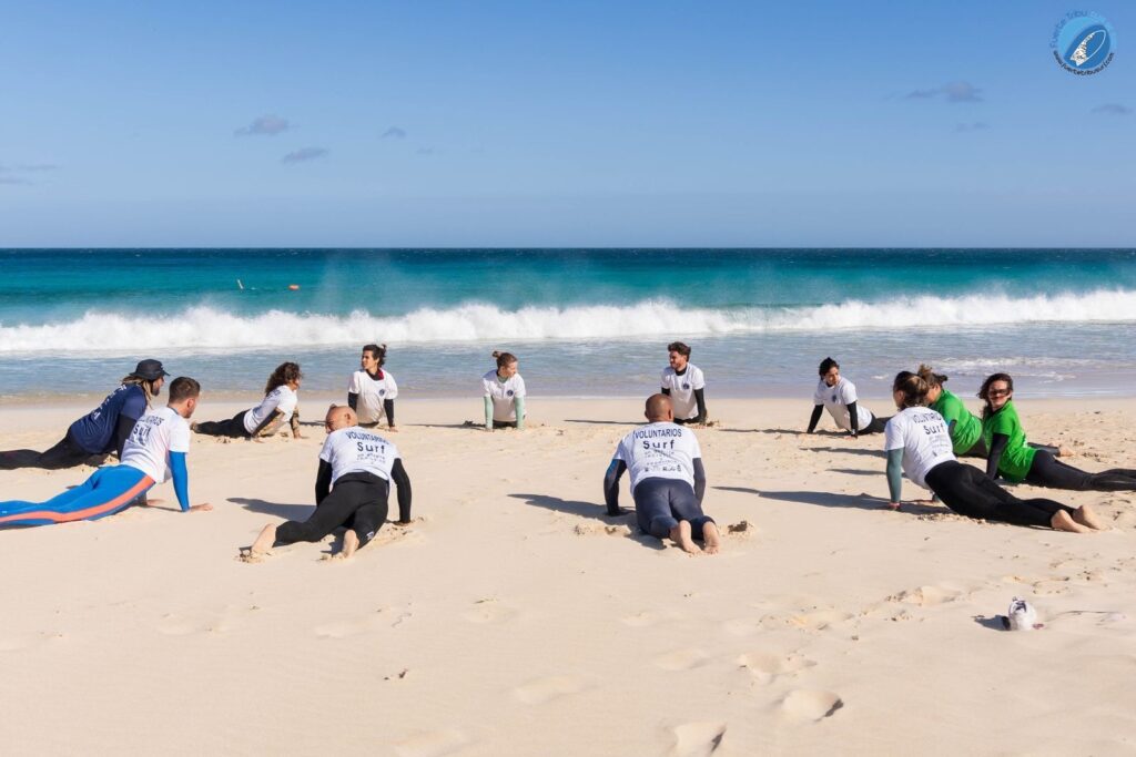 Fuertetribu Clase Surf Principiante 4 1024x683 Una clase de surf de principiantes se acalenta en la playa.