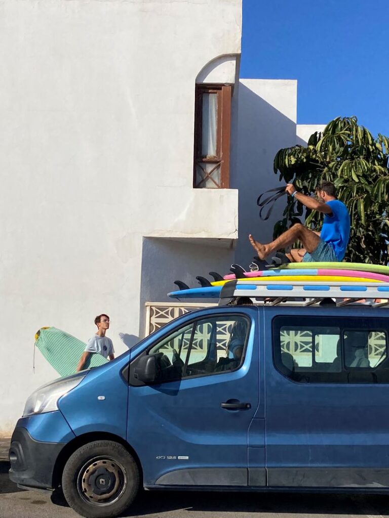 Fuertetribu Surf Para Ninos 40 768x1024 Un monitor está encima de la furgoneta poniendo las cinturas alrededor de las tablas.