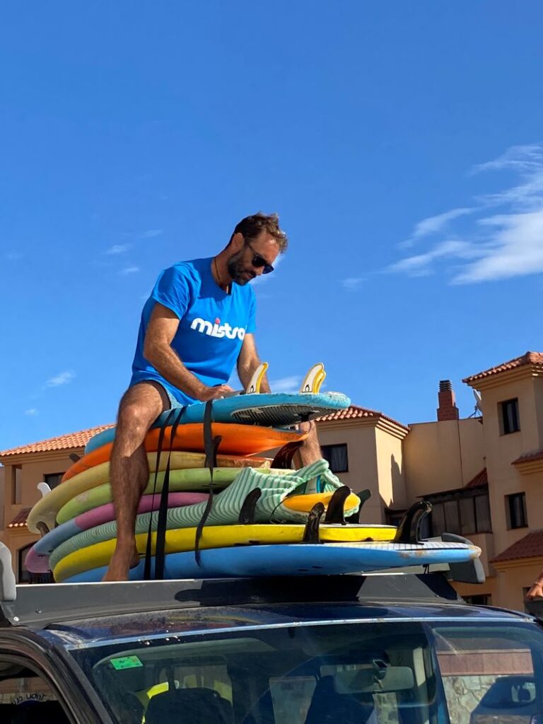 Fuertetribu Surf Para Ninos 41 768x1024 Un monitor fija las tablas en el techo de la furgoneta con cinturas para preparar la clase de surf para niños en Fuerteventura.