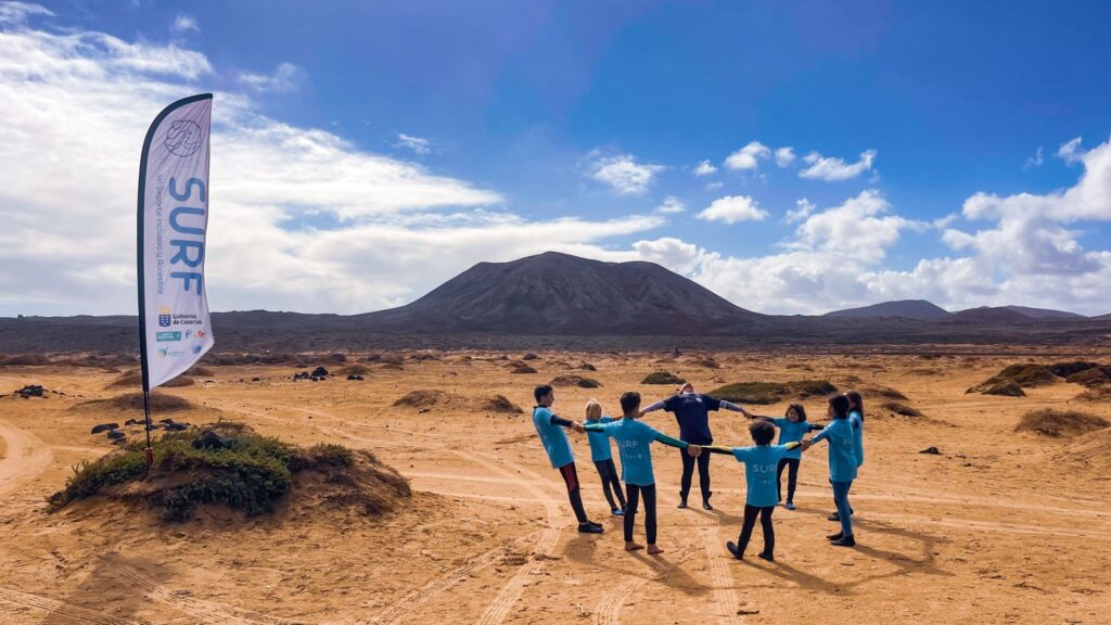 Fuertetribu Surf Para Ninos 6 1024x576 Una monitora de surf y sus estudiantes haciendo un calentamiento antes de una clase de surf para niños en Fuerteventura.