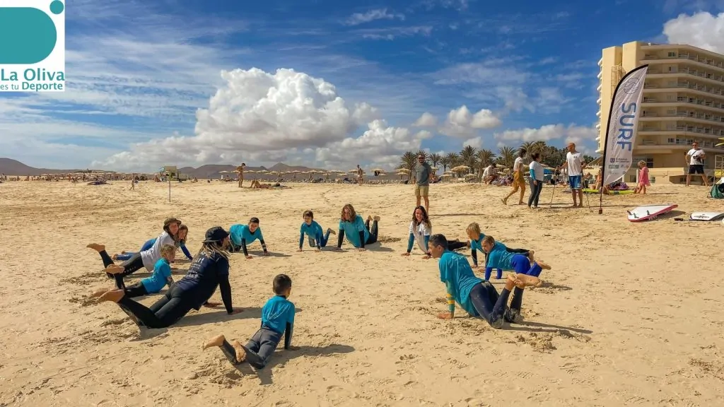 Fuertetribu Escuela Surf Municipal 7 1024x576 Niños haciendo un calentamiento antes de la clase de surf en una playa de Corralejo.