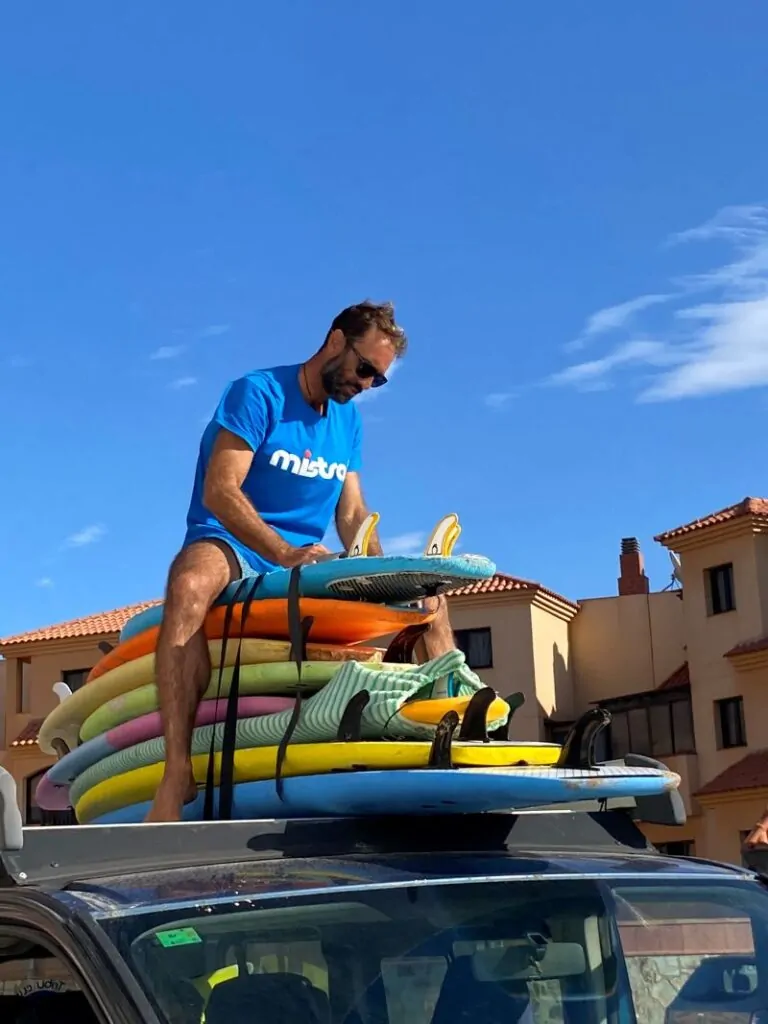 Fuertetribu Surf Para Ninos 41 768x1024 Un monitor fija las tablas en el techo de la furgoneta con cinturas para preparar la clase de surf para niños en Fuerteventura.